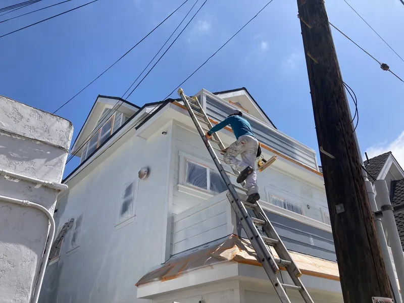 Painter working from a tall ladder on a narrow Coronado lot