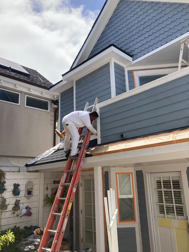 Painter on a ladder painting upper trim on a narrow home