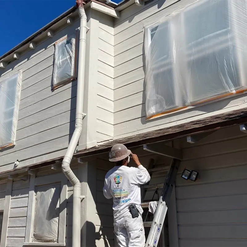 Painter scraping and prepping wood siding on a historic home