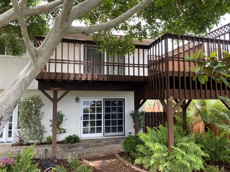 Two-story stucco home with a brown wood deck before repainting in University City