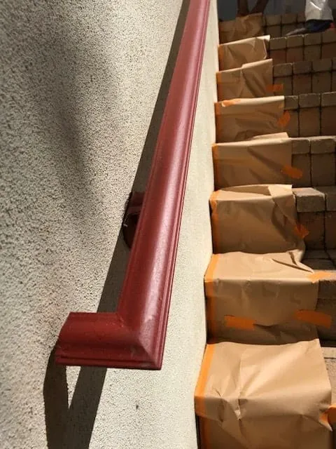 Red handrail being painted along exterior stairs