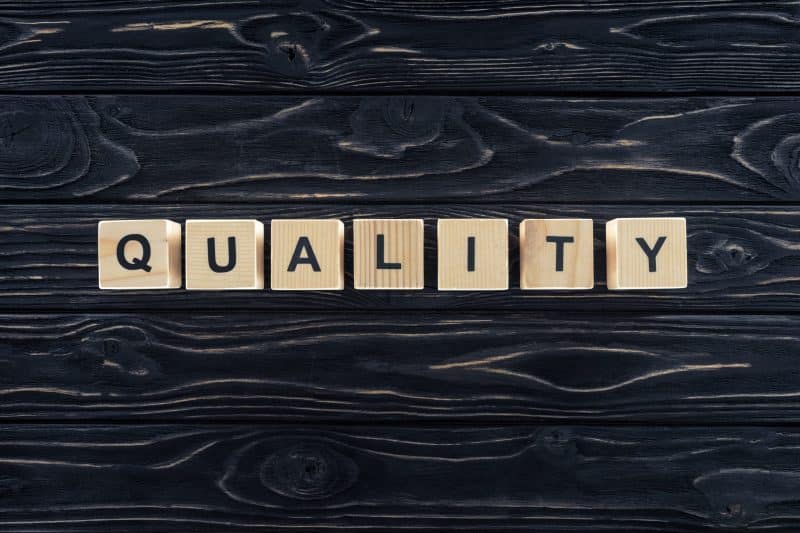 Wooden blocks spelling the word 'QUALITY' on a dark wooden surface