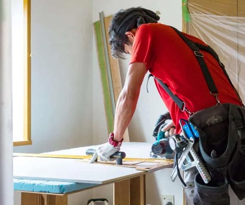 A person measuring and marking a wooden board on a work table.