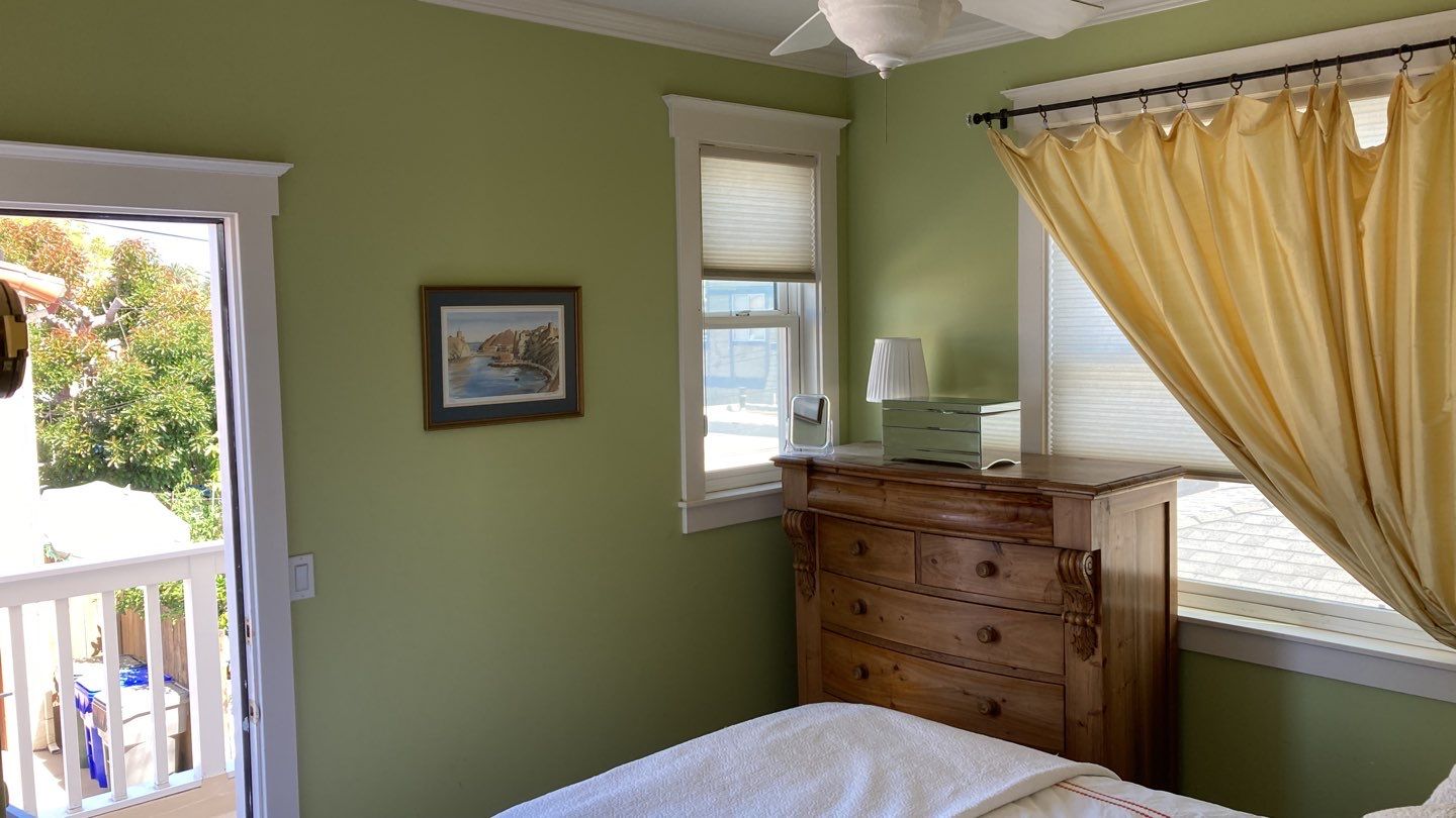 A bright green bedroom with a wooden dresser, yellow curtains, and a window showing outdoor trees.
