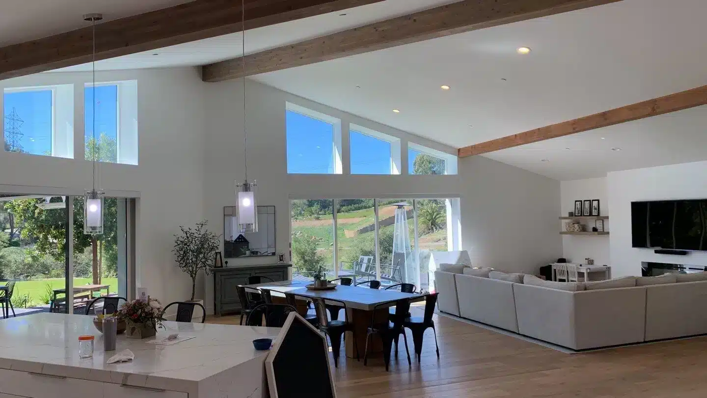 Modern Living Space with Natural Light Spacious, modern living area with large windows, wooden beams, and a dining table.