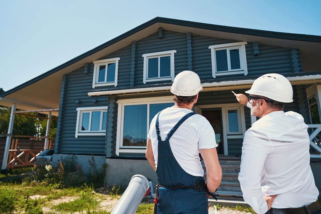 Two contractors in hard hats assessing a home's exterior for painting on a sunny day, ideal for exterior painting in San Diego.