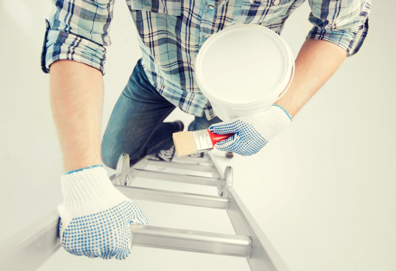 A person on a ladder holding paint and a brush, representing professional House Painters in San Diego preparing for exterior touch-ups.