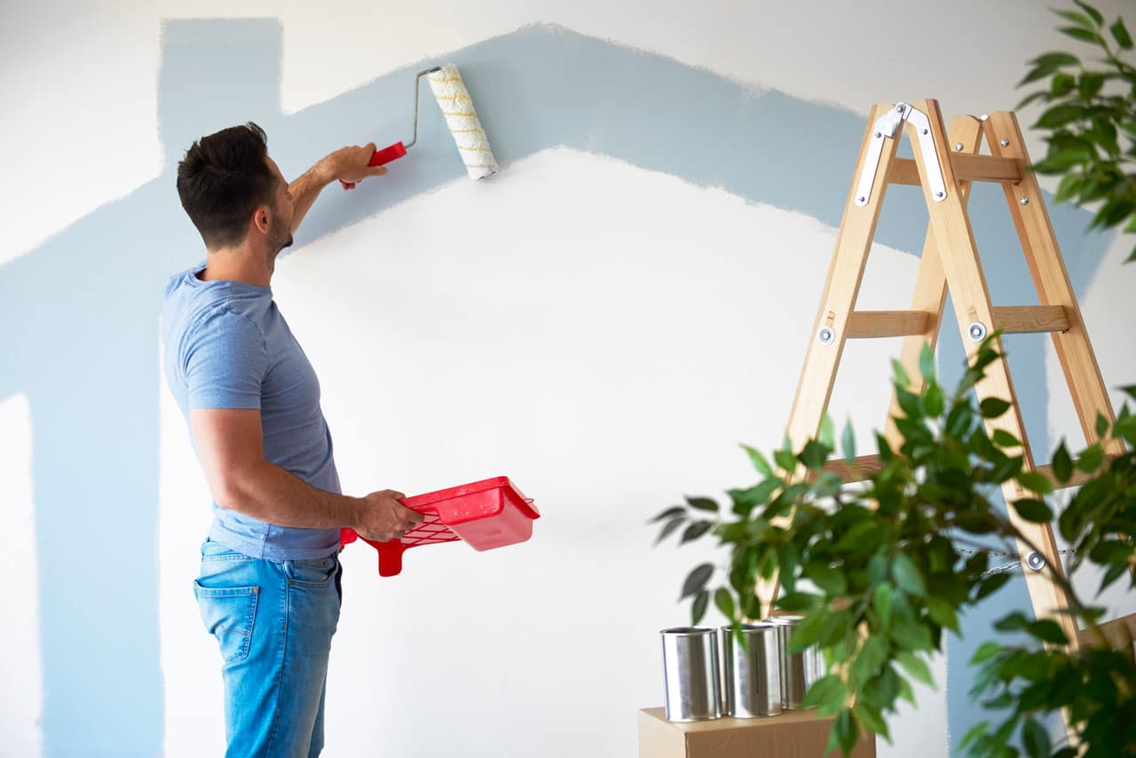 Man painting a house wall with a roller, representing winter maintenance and House Painting in San Diego.