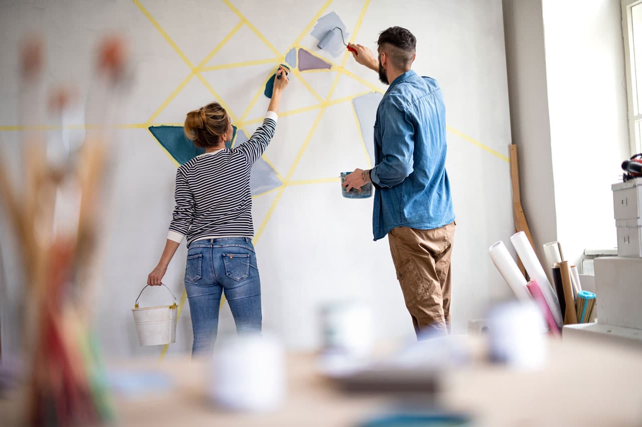 Two people painting a geometric mural on an interior wall, illustrating why homeowners might Schedule Interior Painting in San Diego during winter.